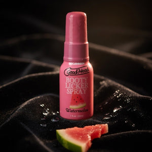 Pink bottle of Goodhead Booty Licker Spray on a grill with watermelon slices.