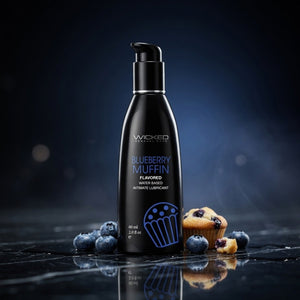 Black lubricant bottle labeled 'Wicked Sensual Care' with blueberries and a blueberry muffin on a dark background