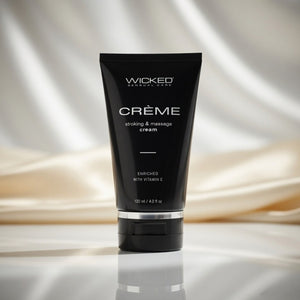 Black tube of Wicked Creème stroking and massage cream on a reflective surface with draped fabric background