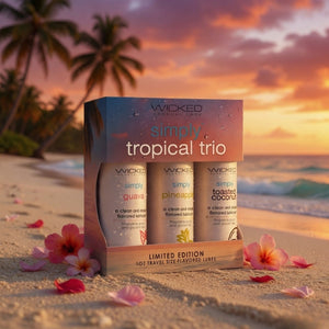 Wicked Simply Tropical Trio packaging on a beach with sunset and palm trees in the background