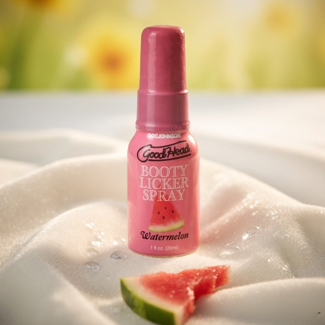 Pink bottle of 'Booty Licker Spray' with watermelon flavor on a white surface with watermelon slices.