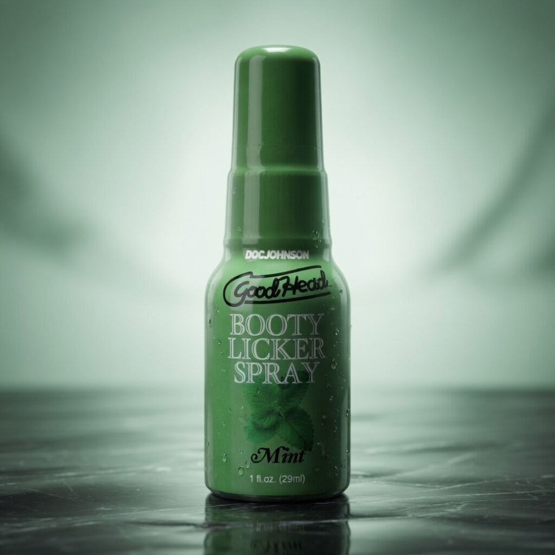 Green bottle of Goodhead Booty Licker Spray on a reflective surface with a gradient background