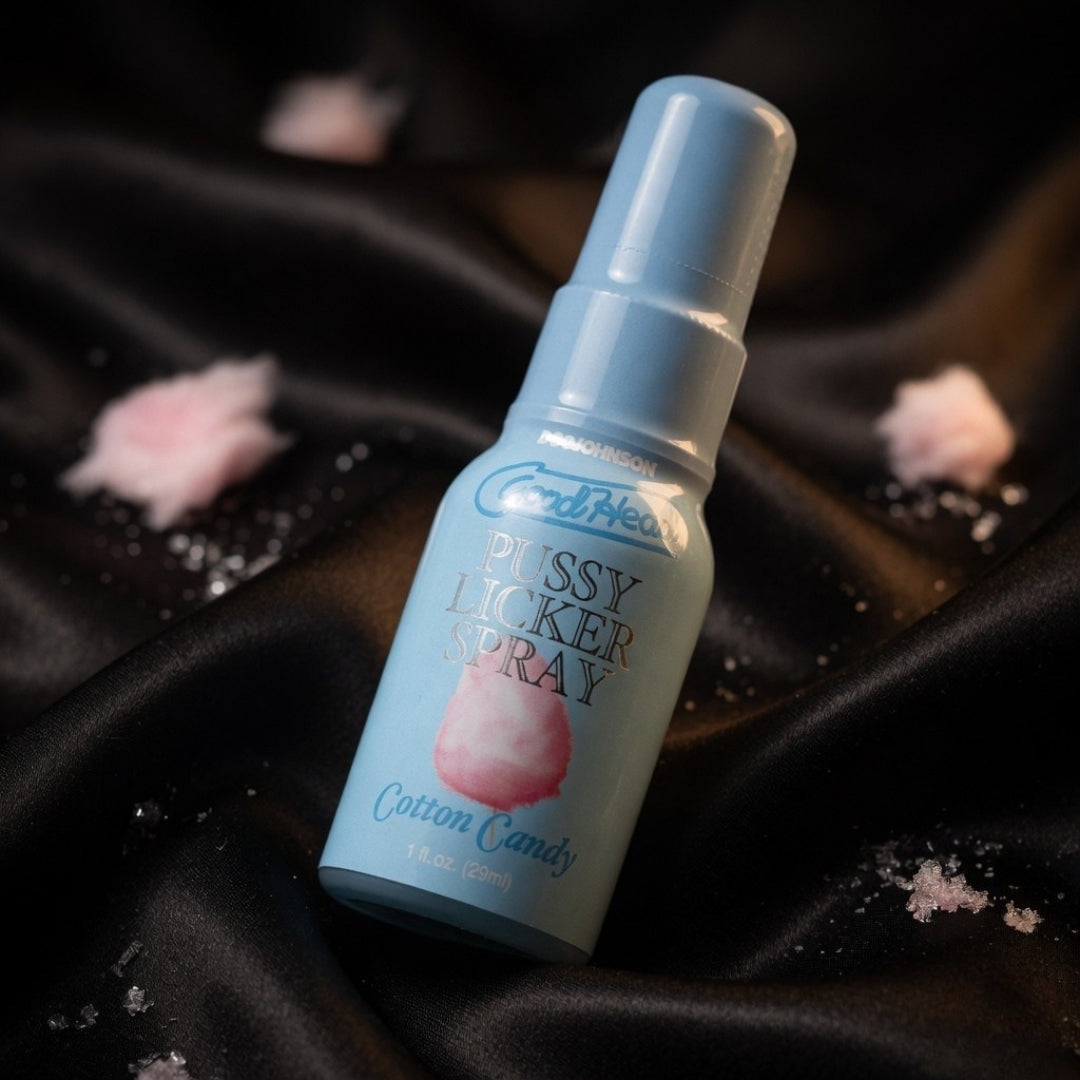 Candylicious Pussy Licker Spray bottle on a black satin background with cotton candy elements.