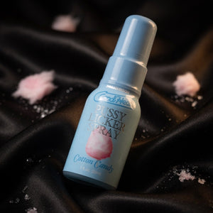 Candylicious Pussy Licker Spray bottle on a black satin background with cotton candy elements.