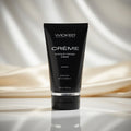 Black tube of Wicked Creème stroking and massage cream on a reflective surface with draped fabric background