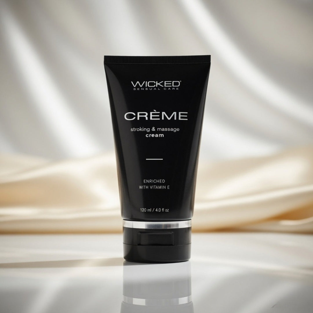 Black tube of Wicked Creème stroking and massage cream on a reflective surface with draped fabric background