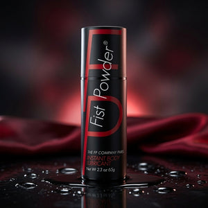 A black cylindrical canister of Fist Powder Instant Body Lubricant with red and white lettering, standing on a glossy wet surface with water droplets and a blurred red satin fabric background.