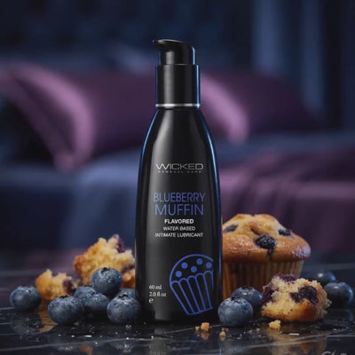 Bottle of Wicked Blueberry Muffin flavored lubricant with blueberries and muffins on a dark surface.